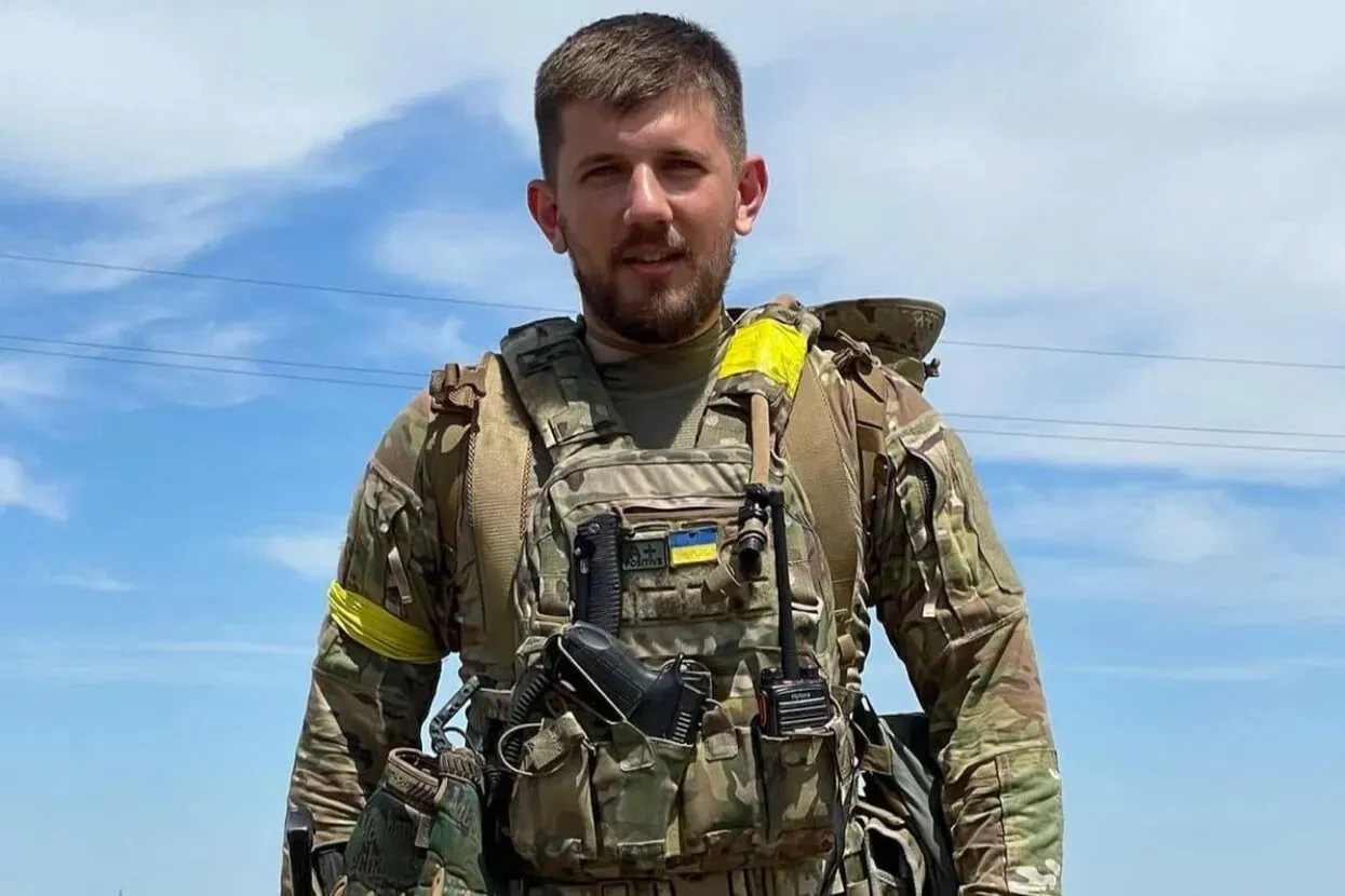 Павло Петриченко у військовому спорядженні з жовтою пов'язкою на тлі неба